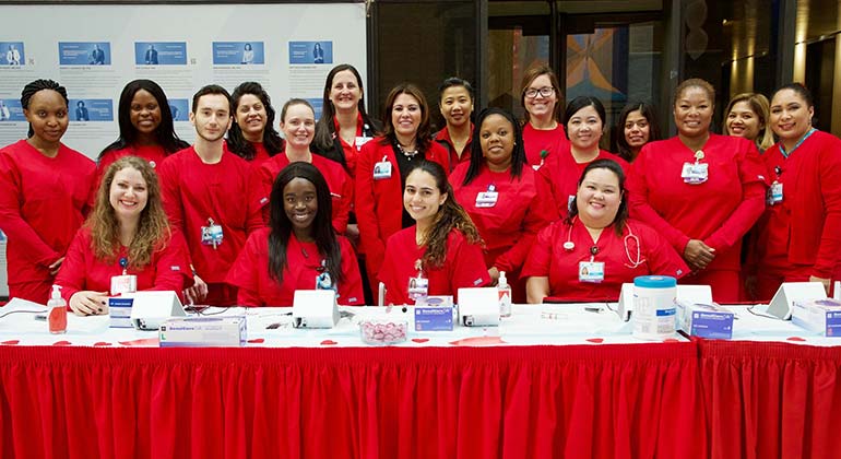 Group of nurses sitting and standing around a table at the annual Go Red for Women event at The Mount Sinai Hospital. All are in red scrubs