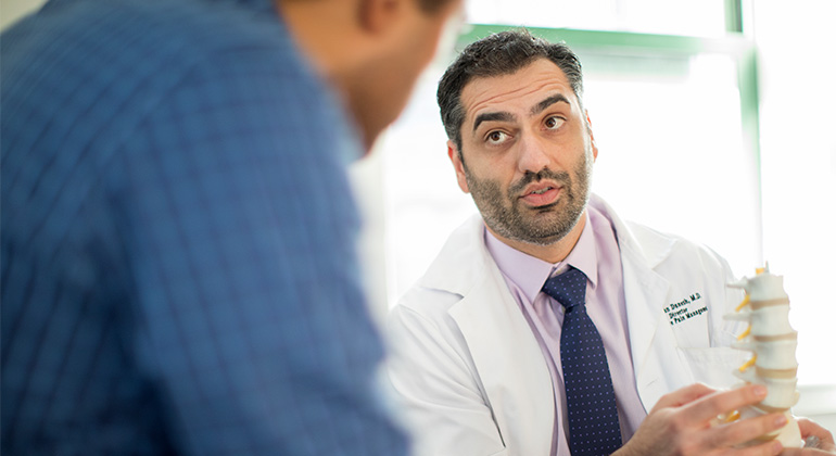 Man talks to doctor, who is seated, wearing a white lab coat, and holding a model spine