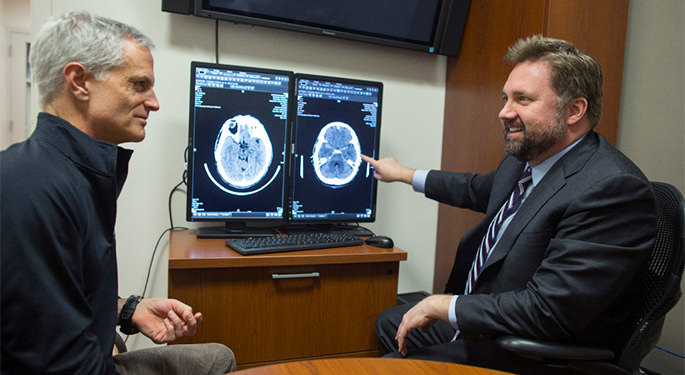 image of Dr. Mocco and patient discussing brain scans on computer screens