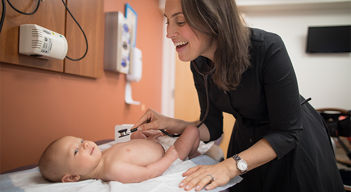 Female doctor examining smiling baby with stethoscope