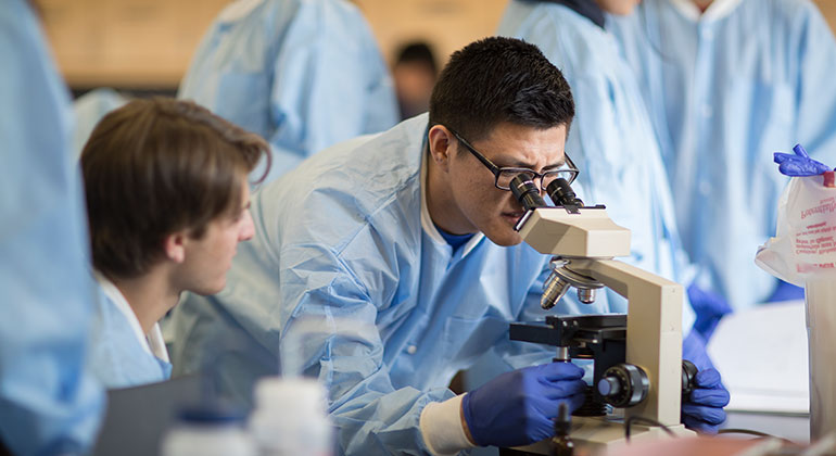 Doctors in a research lab crowded around a doctor using a microscope