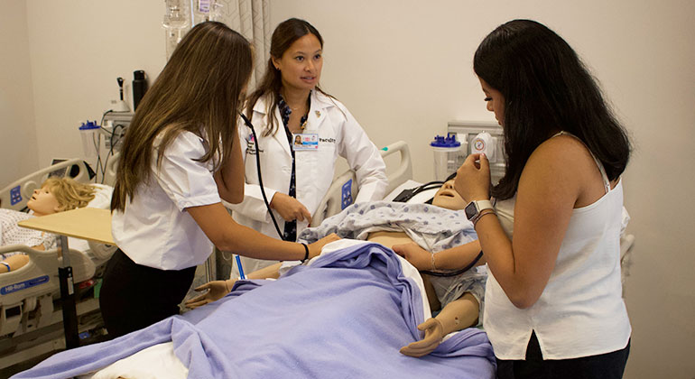 Faculty member mentoring high school students performing an exam on a patient simulator