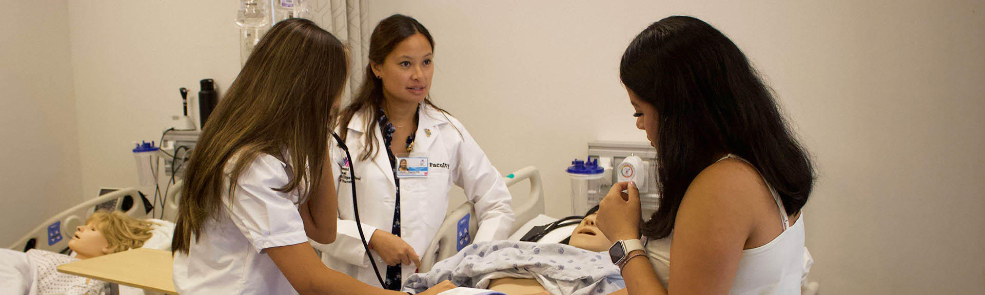 Faculty member mentoring high school students performing an exam on a patient simulator