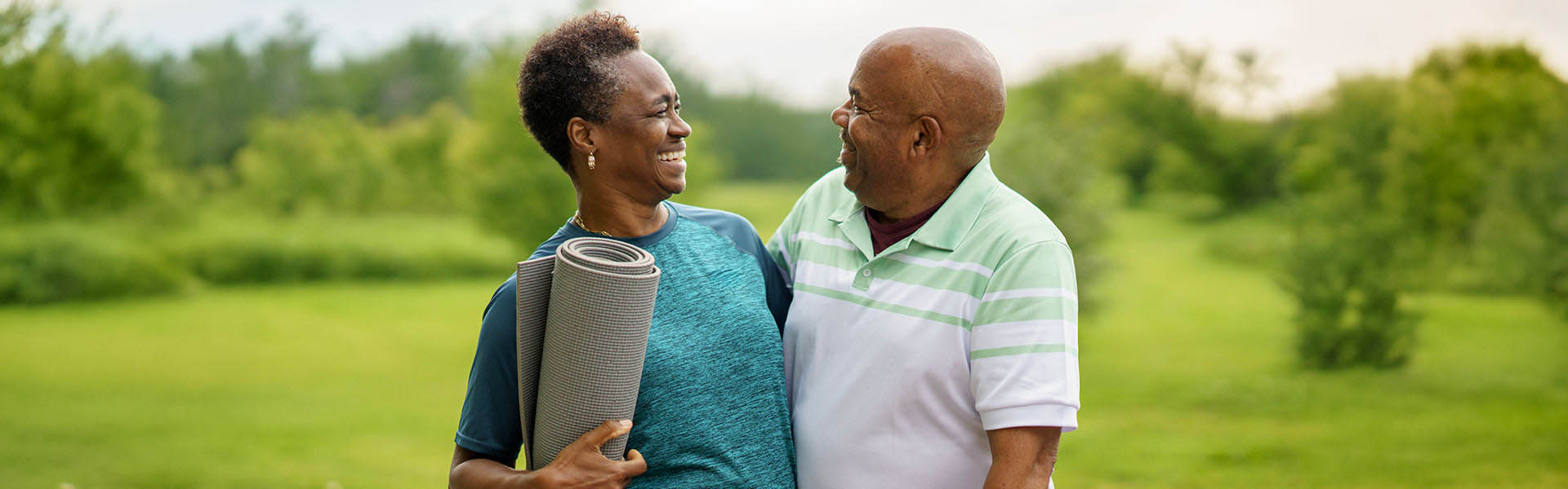 An older man and a women with a yoga mat in hand, side holding each other