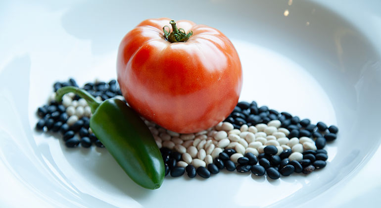 A tomato and jalapeno pepper on top of dried assorted beans in a white bowl