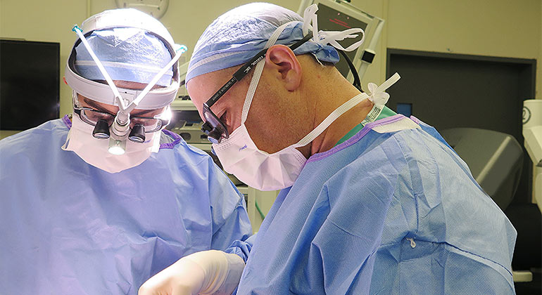 Two surgeons with surgical gear looking down at patient 