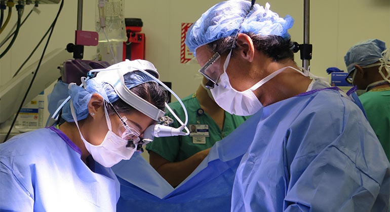 Two surgeons with surgical gear looking down at patient 