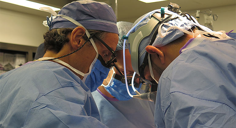 Three surgeons with scrubs in the operating room looking down 