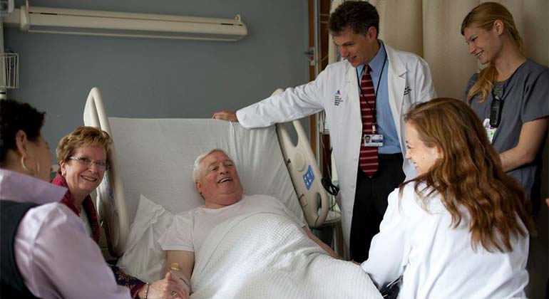 Man in hospital bed surrounded by care team and family