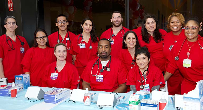 Group of male and female nurses in red sitting at a table posing at an event