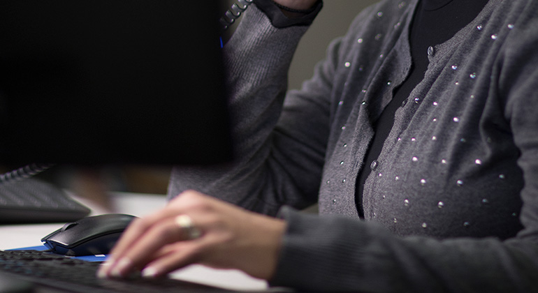Woman wearing gray sweater types on a computer keyboard