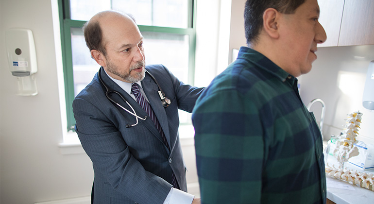 Doctor in a suit, assesses a patient’s back in an exam room