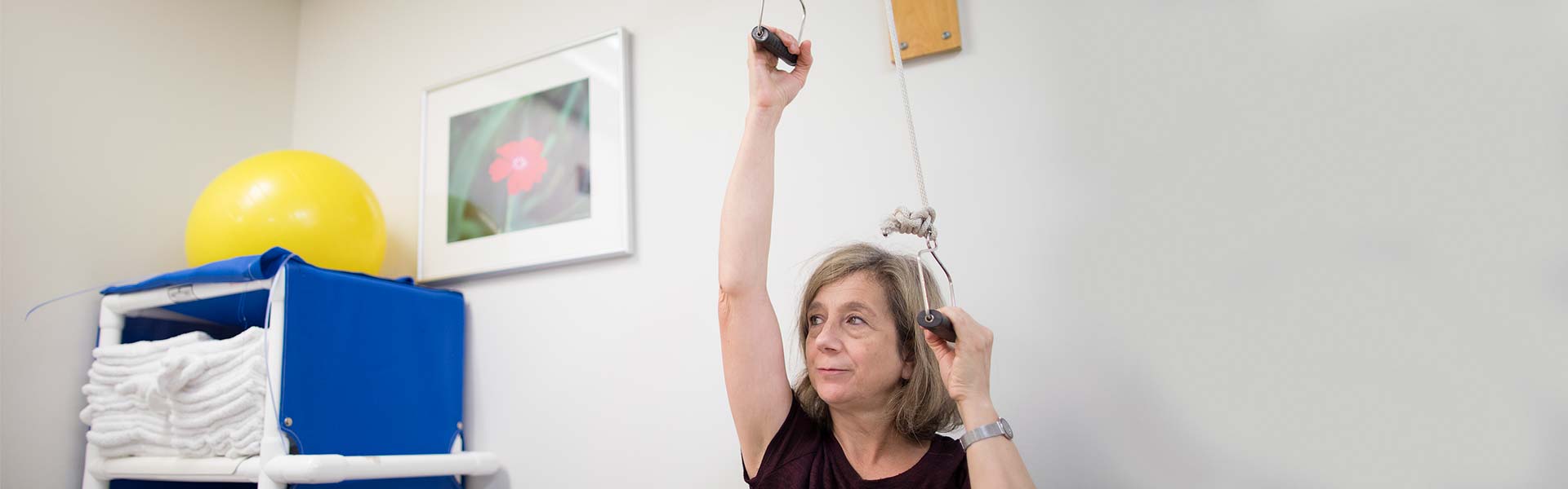 Seated woman works vertical pulleys overhead in exam room