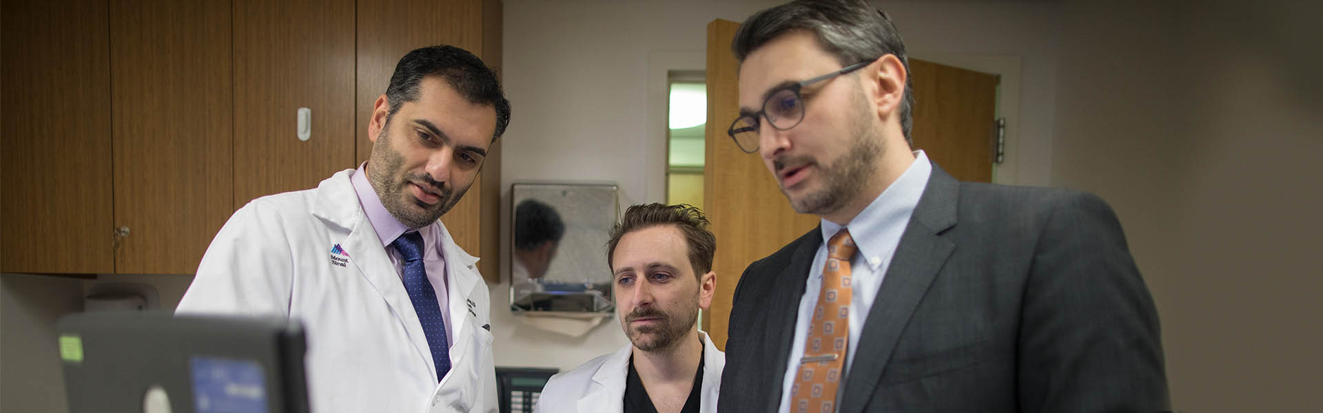 Three doctors stand in an office and look at a computer screen