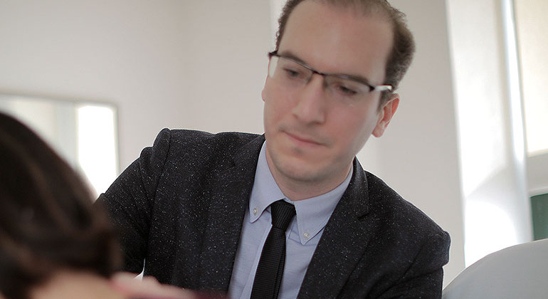 Doctor, in a suit, assesses the back of a woman wearing a purple shirt