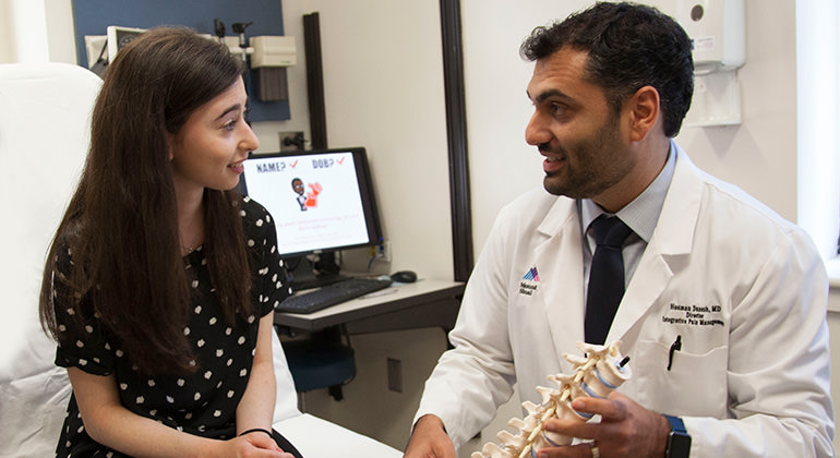 Seated girl in a black and white polka-dotted dress talks to a doctor in a lab coat