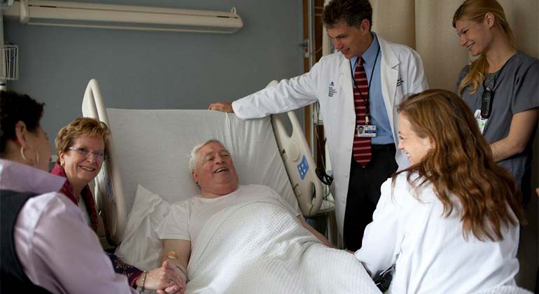 Male patient in hospital bed surrounded by care team and relatives