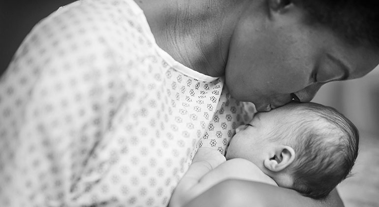 black and white photo of a mother lightly kissing the forehead of her baby