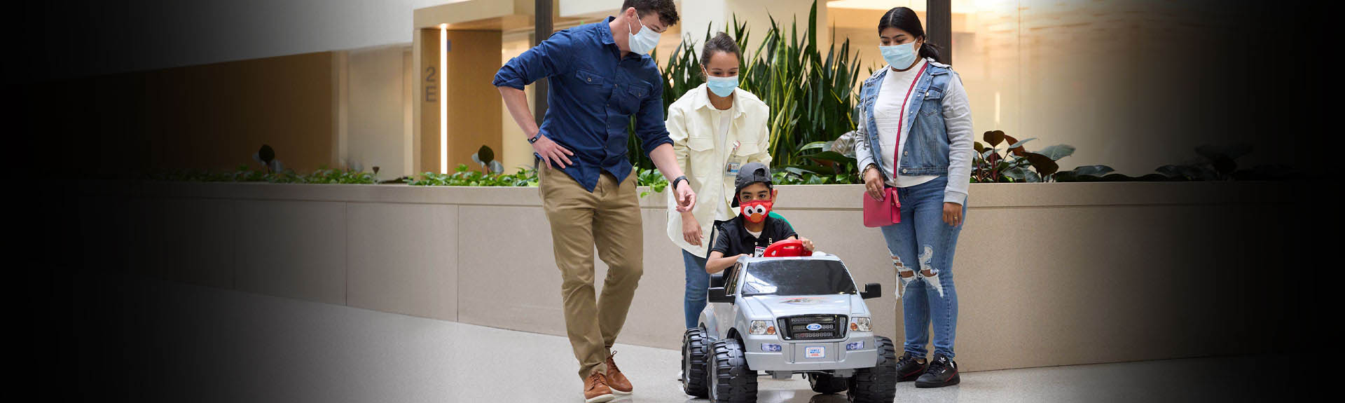 child in toy car next to two individuals