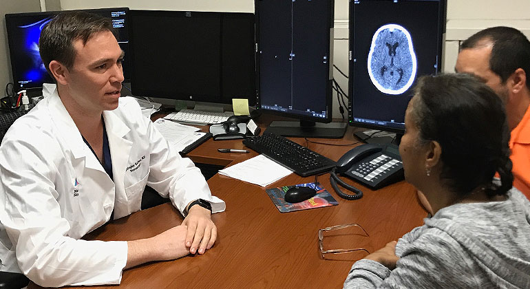 doctor sitting across from desk talking to patient and family member 