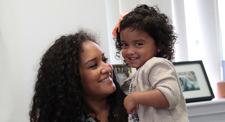 A woman smiling while holding her smiling toddler daughter