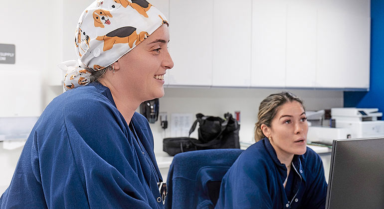 Two female nurses at nurses station talking to someone not pictured