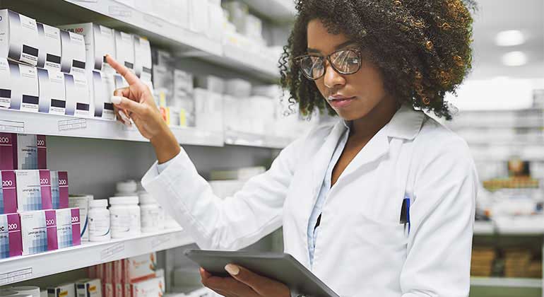 Pharmacist with clipboard checks medicine on shelf