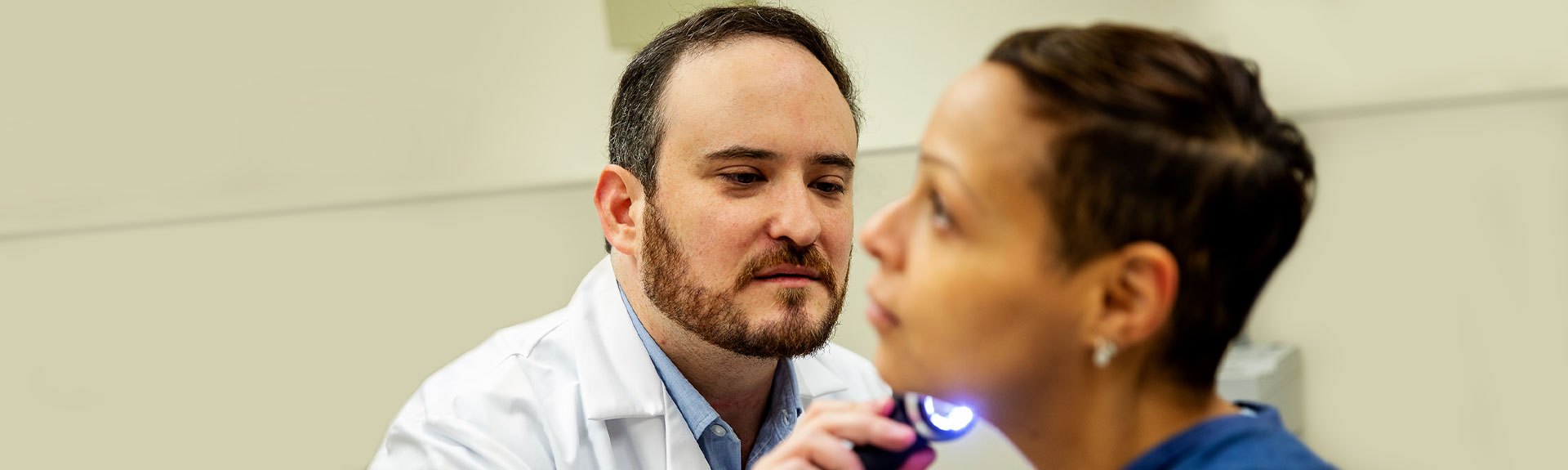 Male physician examining a female patient using a dermatoscope