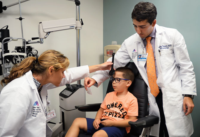 A photo showing Erin Walsh, MD, with a NYEE pediatric ophthalmology fellow, Phillip Tenzel, MD, performing a cover test for ocular misalignment.