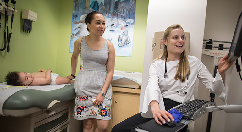 Doctor looking at computer screen and talking with mom standing next to baby on examining table