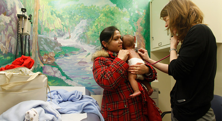 Doctor examining baby being held by mom in emergency room