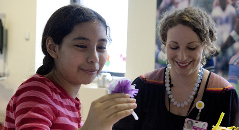 Young girl making paper flowers sitting next to social worker