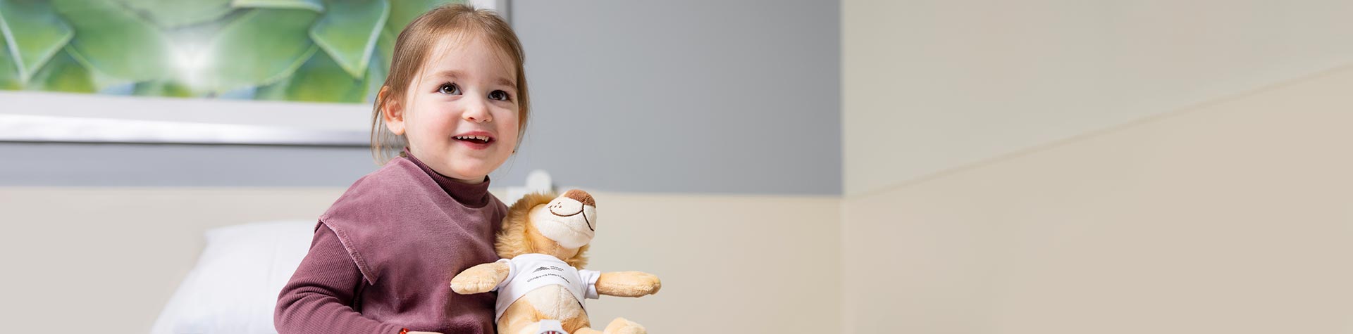 Toddler patient, smiling holding Kravis Children Heart Center plush animal