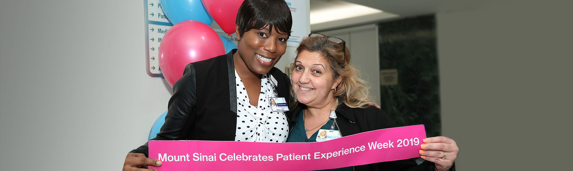 Two women hold up a sign that reads" Mount Sinai Celebrates Patient Experience Week 2019"