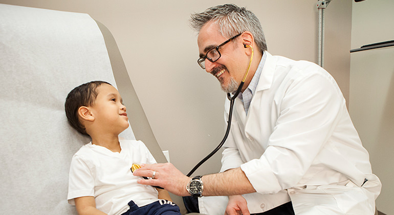 doctor examining child using a stethoscope while on patient bed