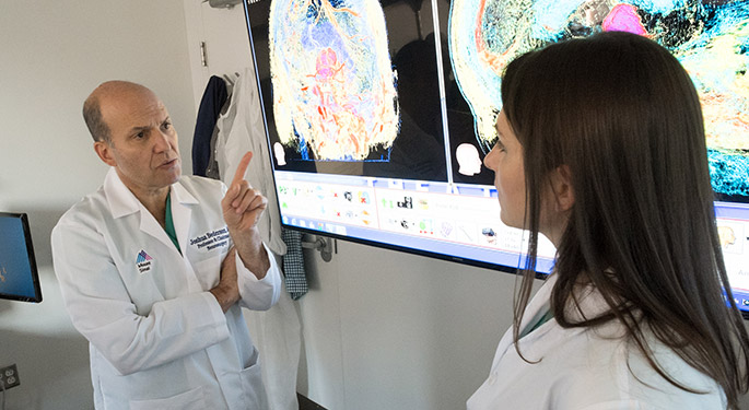 doctor explaining and demonstrating to another staff member medical results from a screen