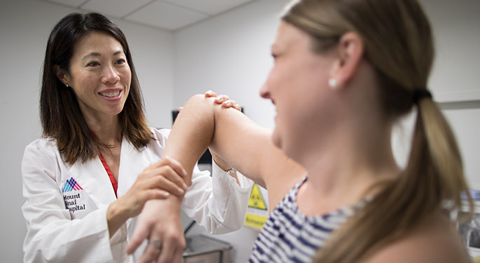 Dr. Alexis Colvin examining female patient’s elbow during office visit