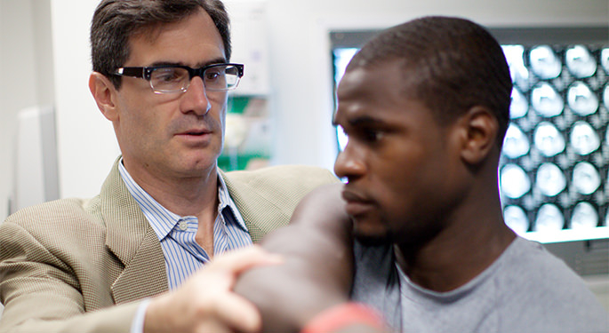 Dr. James Gladstone examining male patient’s shoulder and elbow during office visit