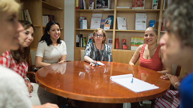 Several women sitting at round table talking and listening in library