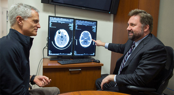 image of Dr. Mocco and patient discussing brain scans on computer screens