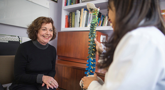 image of nurse discussing diagnosis with patient in an office setting while holding spine model
