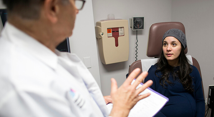 Seated pregnant patient talks with doctor