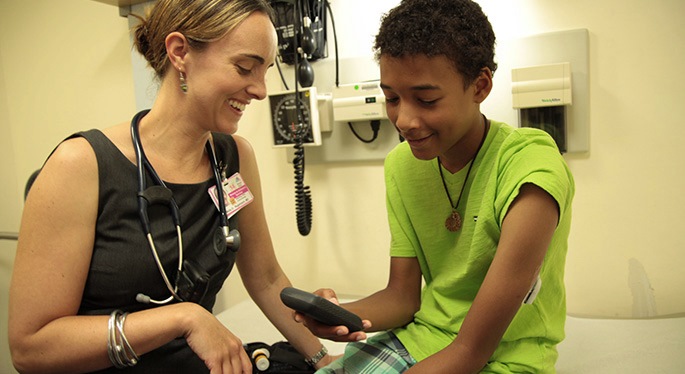 Smiling child and doctor looking at diabetes monitor