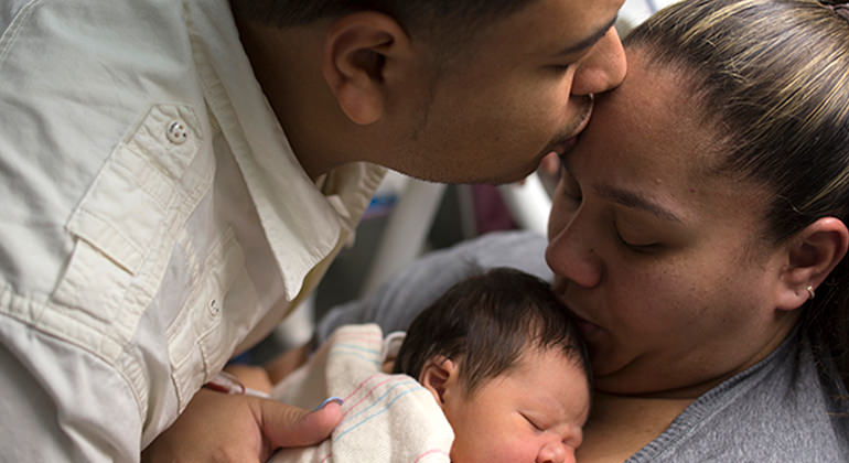 Mom holding newborn baby while husband kisses her forehead