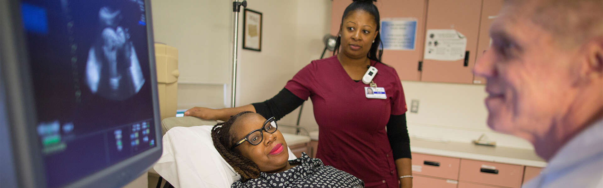 Doctor performing sonogram on pregnant woman with nurse by side