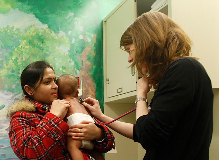 Photo of Doctor examining baby being held by mom in emergency room