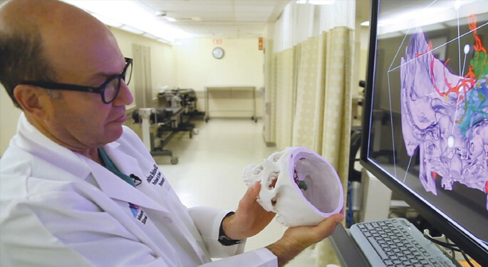 image of Dr. Bederson reviewing 3D model brain, comparing to brain scan on computer screen