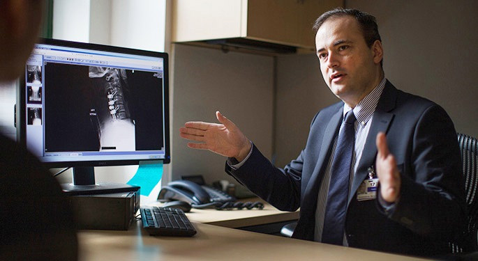 image of physician reviewing x-ray on computer screen, in discussion with patient in office setting